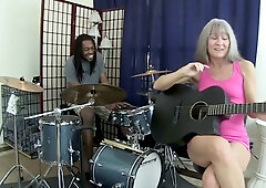Blonde woman with gray hair takes black musician deep in throat and bed