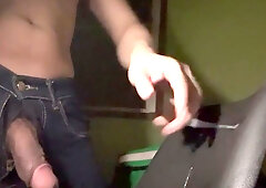 A toned man unzips his jeans to expose his erect penis in a dimly lit room