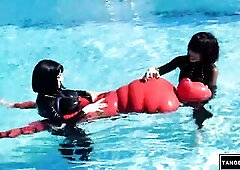 2 hotties in ebony latex catsuits stand in an outdoor pool, handling and floating a person totally encased in glossy red latex with ebony belts on an 