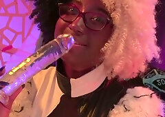 Dark-skinned woman with glasses takes a glossy dildo deep while bent over a stool