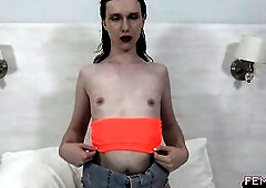 Trans woman in matching orange top and pink haunch-high nylons kneels, widens, and inserts an orange sex tool on a bedroom couch with white sheets.